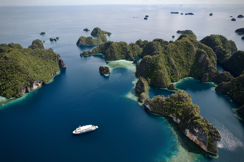 Aerial view of Kudanil Explorer yacht cruising through the turquoise waters of Raja Ampat, Indonesia.