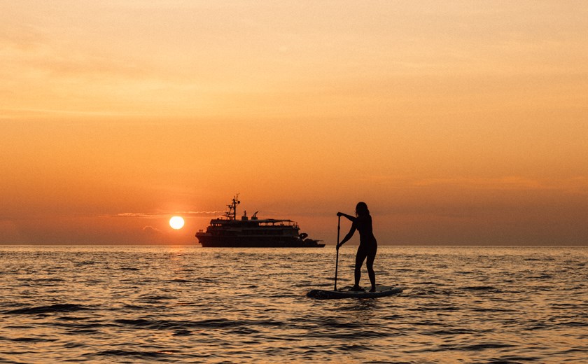 Guest paddling at sunset during a private yacht expedition through the Indonesian islands.