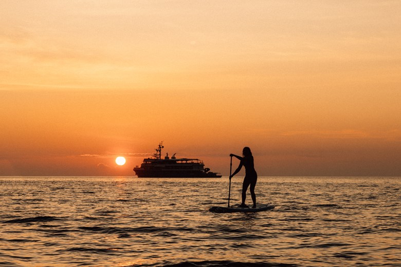 Guest paddling at sunset during a private yacht expedition through the Indonesian islands.