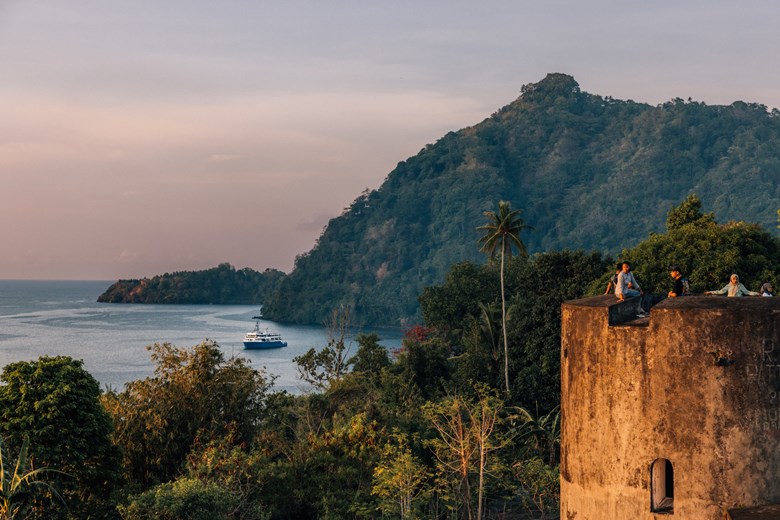 View of the Spice Islands with the Kudanil Explorer yacht anchored below, children watching the view from above during a private yacht expedition in Indonesia.