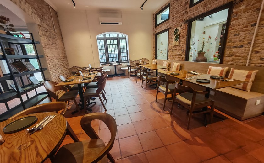 Interior of a farm-to-table restaurant in George Town, Penang, with wooden tables and chairs, large windows, and a cozy dining atmosphere.