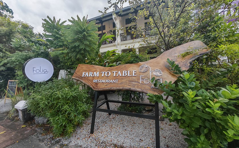 Entrance of a farm-to-table restaurant in George Town, Penang, surrounded by lush greenery and a wooden sign reading ’Farm to Table’